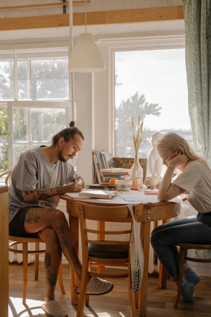 Two young adults engage in study at a sunlit table, creating a serene learning environment.